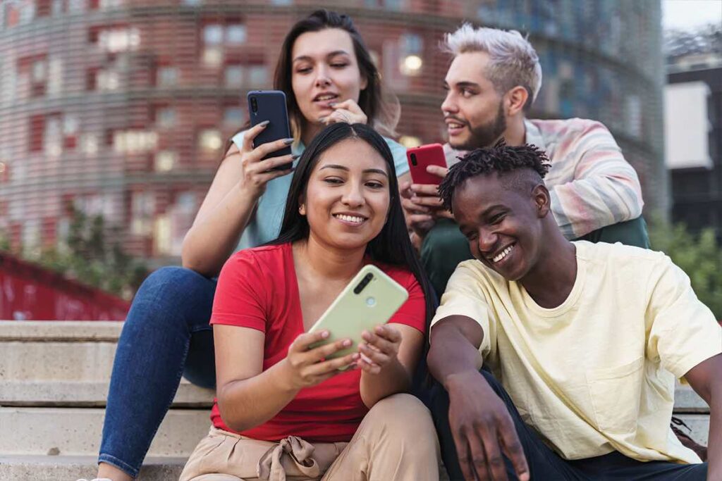 Images showing 4 students looking at content on their mobile phones together Roksta Media Services